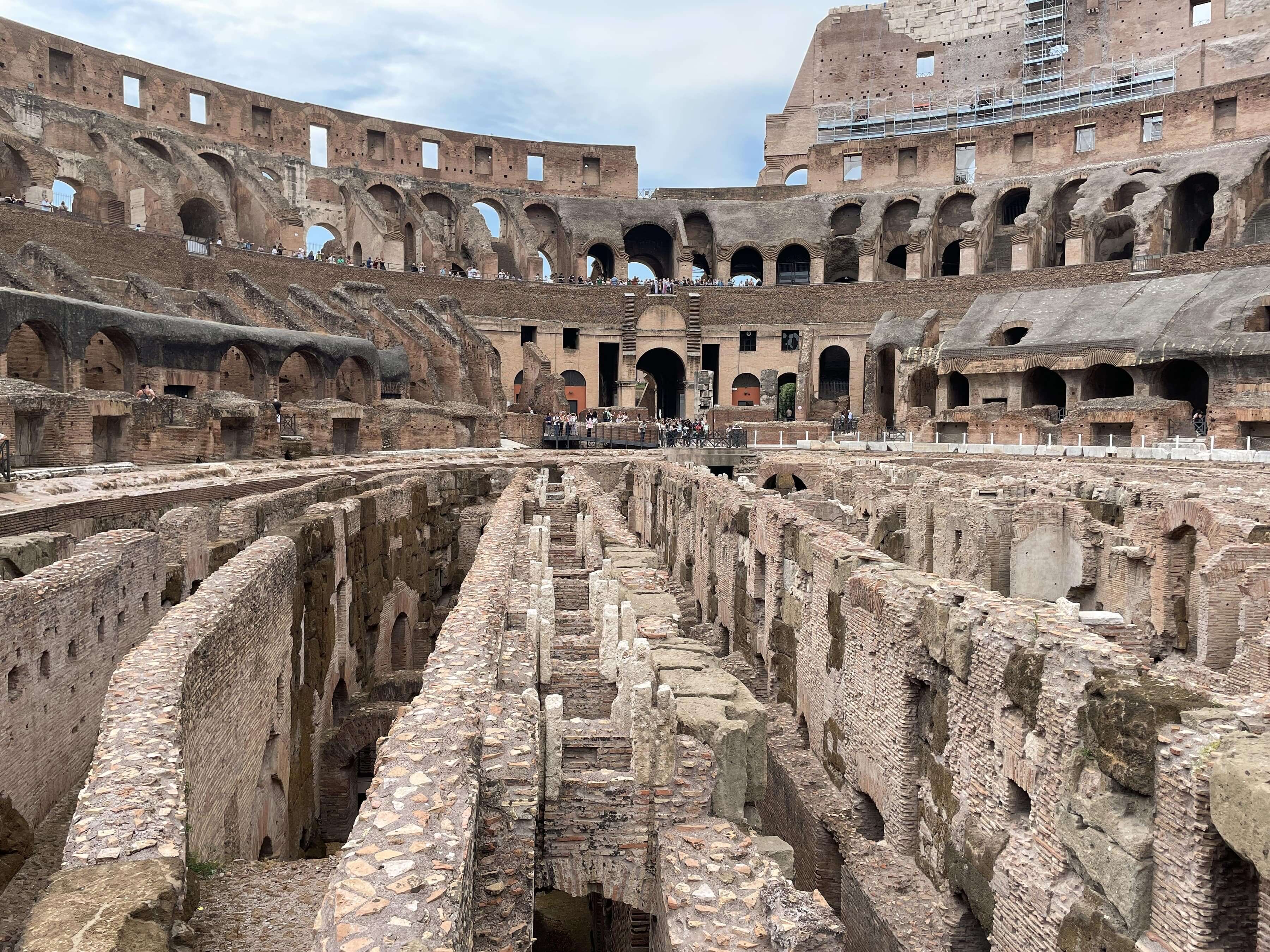 Overview of the inside of the Rome Colosseum, looking down on the underground area and dungeons, with many tourists.